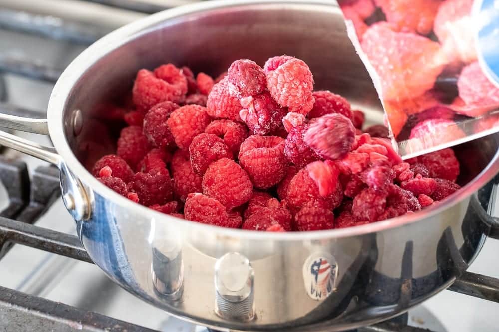 The Best Thick Raspberry Sauce | Family Cuisine 3 woman adding sugar to frozen raspberries for sauce