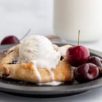 Mini cherry galette on a black plate with ice cream on top.