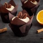 Gingerbread cupcakes with orange buttercream on the table with cinnamon sticks and oranges.