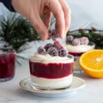 Woman adding sugared cranberries on top of white chocolate mousse.