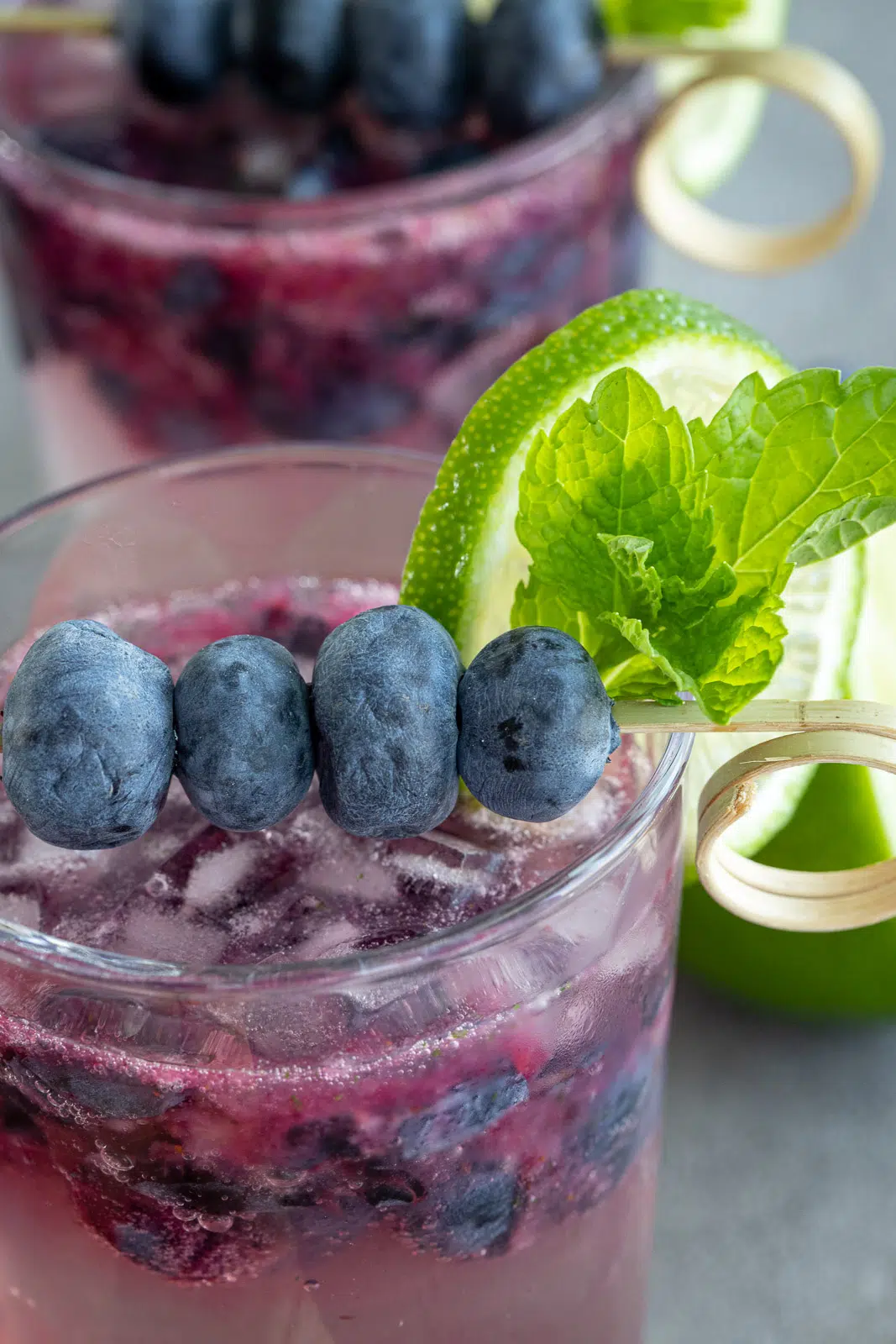 A glass of nonalcoholic blueberry mojito with blueberries, a lime wedge, and mint for garnish