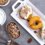 Simple baked peaches on a white tray topped with yogurt and granola.