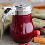 A jar of cranberry syrup on the table with fresh cranberries.