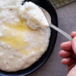 Woman scooping grits off a black plate with an antique spoon.