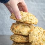 Woman holding a green chili biscuit in a stack on a surface,