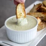 Woman dipping roasted potatoes into habanero ranch dressing in white dish.