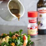 Woman pouring poppy seed salad dressing recipe over a kale salad.