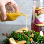 Woman pouring red wine vinaigrette over a kale salad.