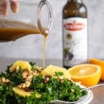 Woman pouring a citrus balsamic vinaigrette dressing over a kale salad.