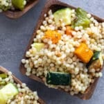 Pearl couscous salad with roasted vegetables in wooden bowls.