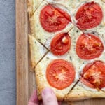 Herb ricotta tomato puff pastry tart cut into diamond shapes on a wood cutting board.