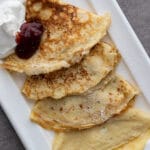 Pannkakor Recipe (Swedish Pancakes) on a white platter with whipper cream and strawberry jam.