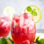 Raspberry mojito mocktail in a glass with fresh raspberries on the surface and mint leaves.