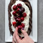 Woman placing cherries on top of a chocolate bundt cake.