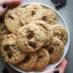 Chocolate chunk cookies on a white plate a woman is holding.