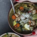 Woman holding a ceramic bowl of vegetable barley soup.