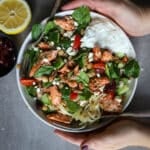 A woman's hands wrapped around a salmon bowl with farro.