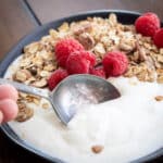 Bowl of homemade greek yogurt in a bowl with a spoon dipping a bite.
