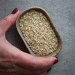 A woman holding a small ceramic bowl of brown rice.