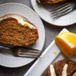Carrot cake with orange glaze on white plates and white platter.