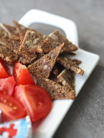 Rye chips on a white platter with sliced tomatoes and Laughing Cow cheese.