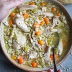 Woman holding a ceramic bowl of chicken and barley soup.
