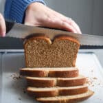 Woman slicing homemade rustic spelt bread on a plastic cutting board.