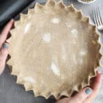 Woman holding a rye pie crust in a glass pan.