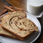 2 slices of whole wheat cinnamon raisin swirl bread on white plate with milk in the background.