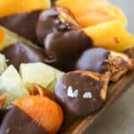 Dried fruits dipped in dark chocolate in a wooden bowl.
