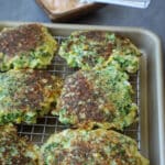 Broccoli corn fritters on a cooling rack on a sheet pan with spicy mayo next to it.