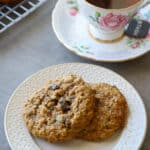 Muesli cookies on a white plate with a cup of tea in an antique cup beside it.