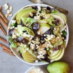 Pear salad with feta in a white bowl with cinnamon sticks on the side and pear.