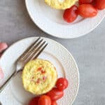 Baked hashbrown egg cups on white plates with tomatoes on the side with forks on each plate.