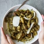 Pesto gnocchi in a white dish topped with slices of parmesan.