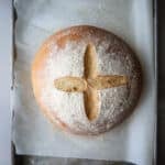 Scored potato bread on a lined baking sheet.