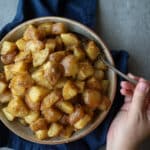 Slow cooker potatoes in a ceramic bowl with a woman holding a spoon on the side.