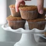 Woman taking a zucchini bran muffin from a white cake stand.