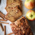 Cinnamon apple bread on a piece of parchment paper with apples and cinnamon sticks beside it.