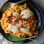 Pumpkin risotto on a black plate with fresh sage on the side.