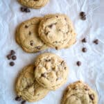 Chocolate chip cookies on a piece of parchment paper with chocolate chips on the side.