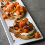 Roasted butternut with bacon on crostini on a white platter.