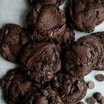 Dark chocolate and dried cherry cookies in a pile on a piece of parchment paper.