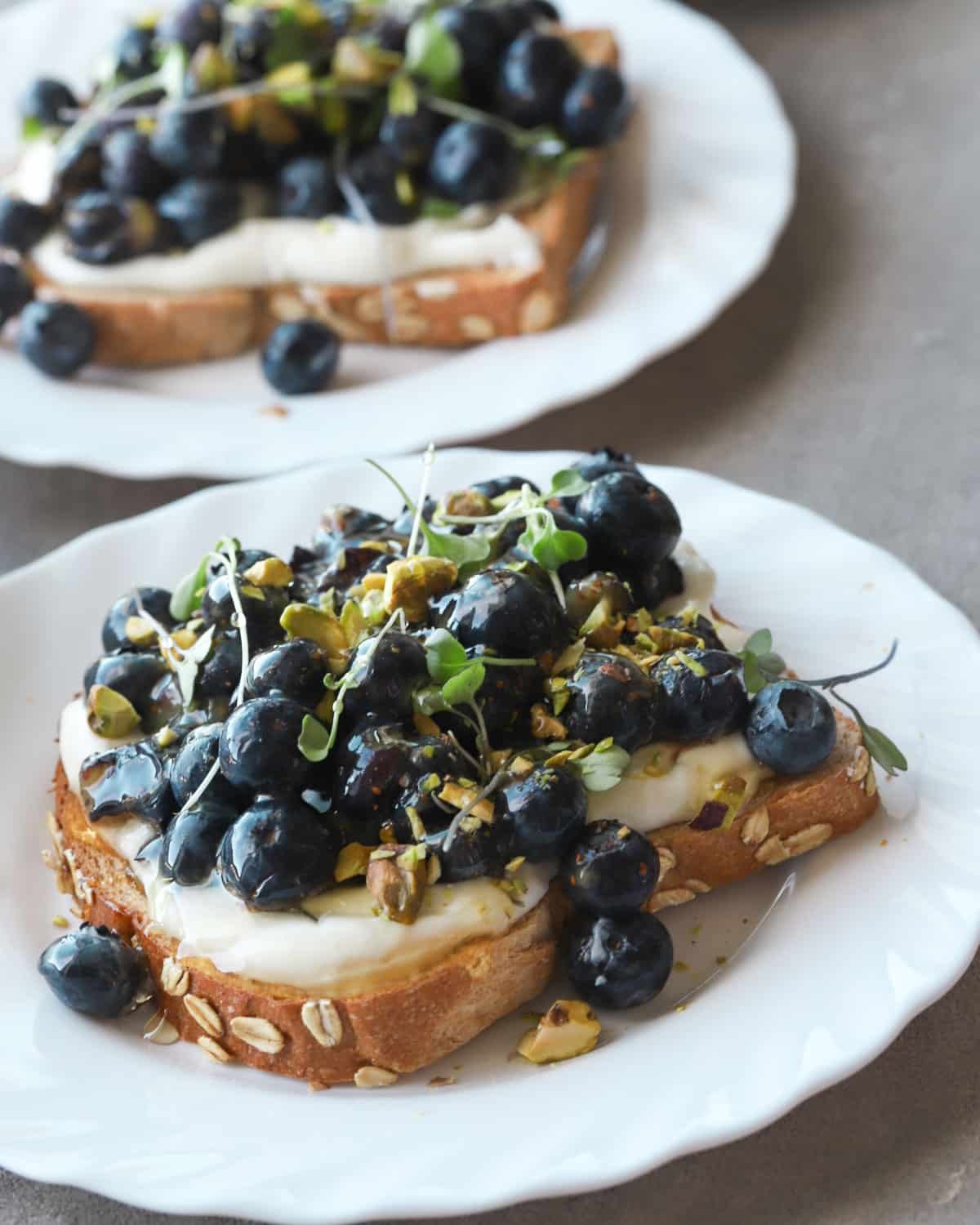 Ricotta and blueberry toast on a white plate topped with pistachios.