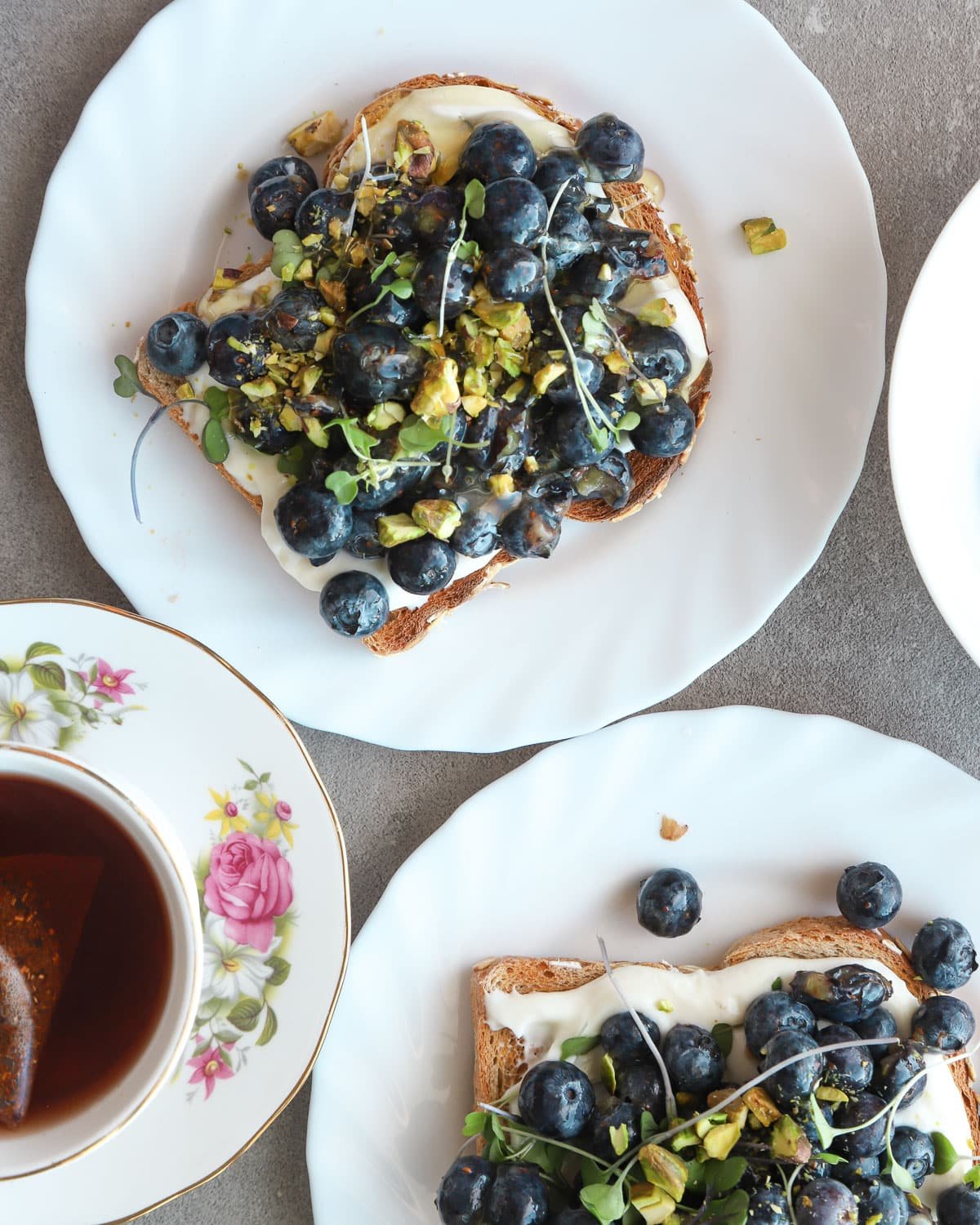 Blueberry toast on two white plates with a cup of tea in an antique cup next to it.