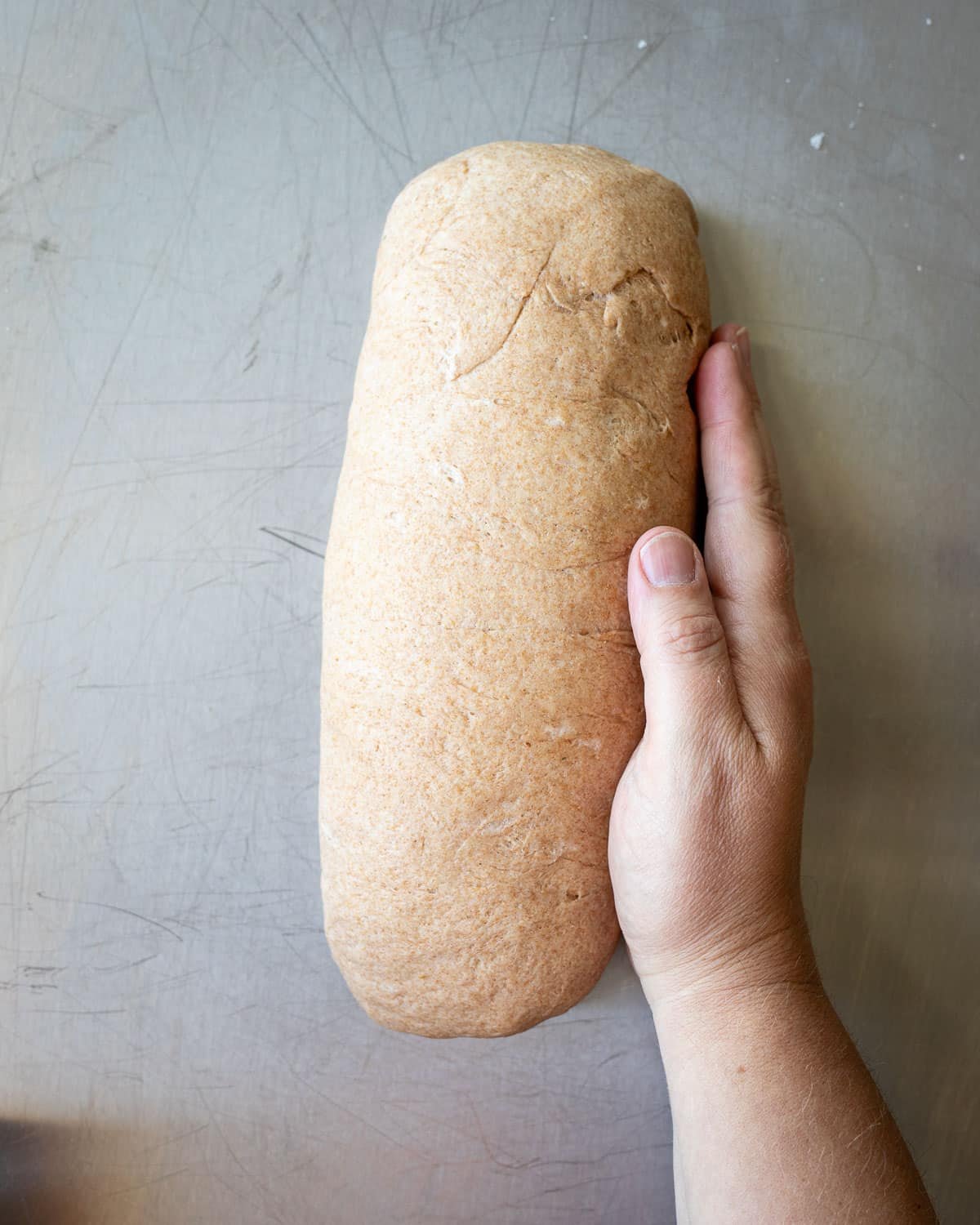 Woman shaping a loaf of bread on a metal surface.