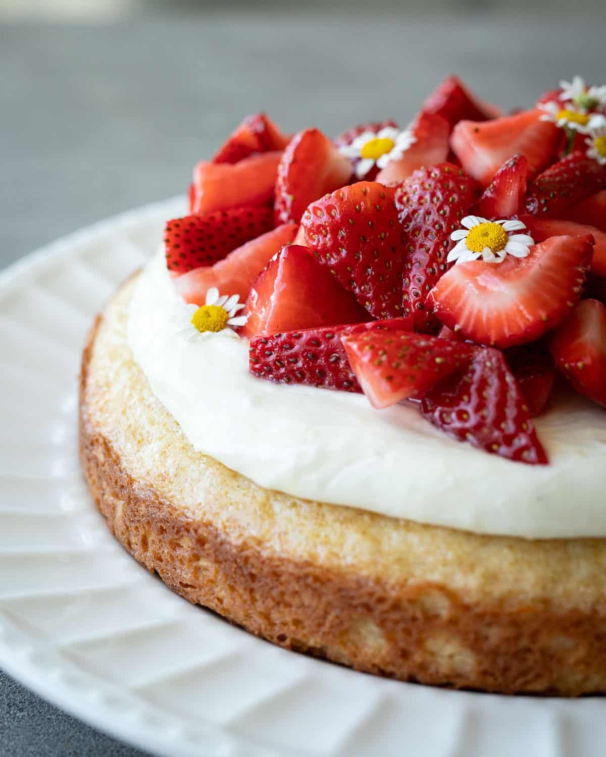 Chamomile cake with cream cheese icing topped with strawberries on a white plate.