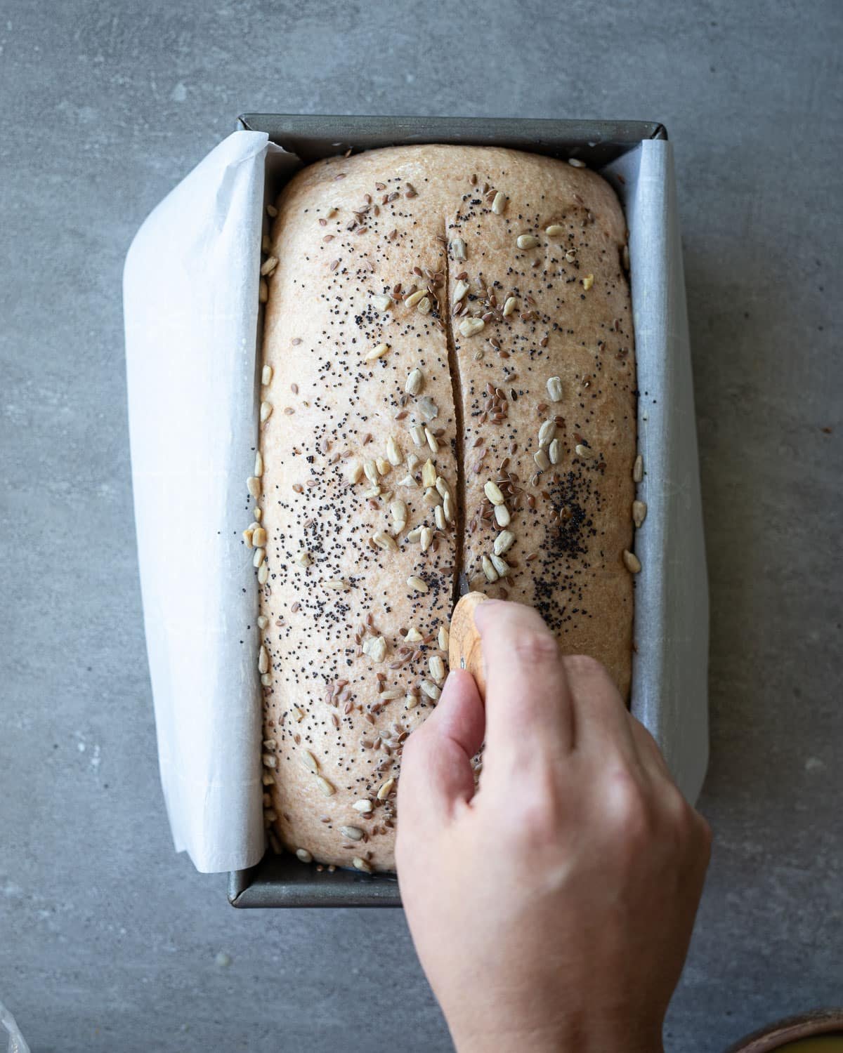 Woman scoring a loaf of bread in a loaf pan.