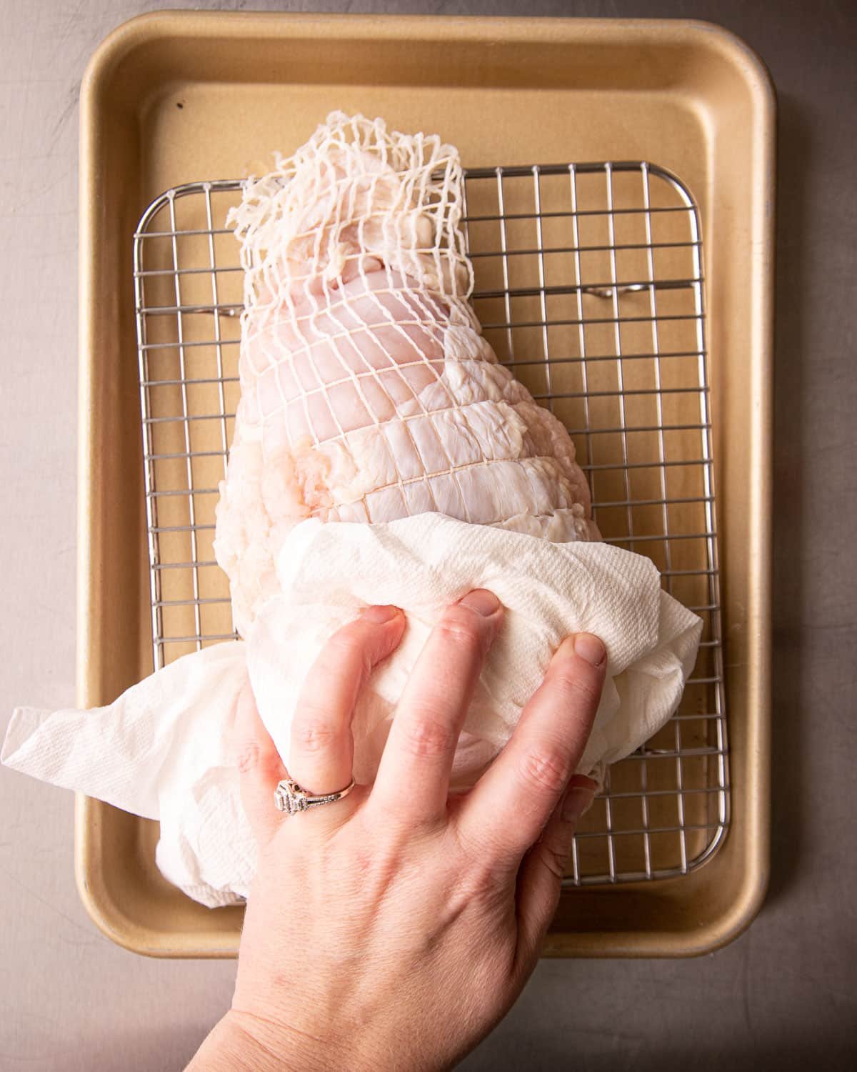 Woman patting dry a turkey breast on a cooling rack on a pan. 
