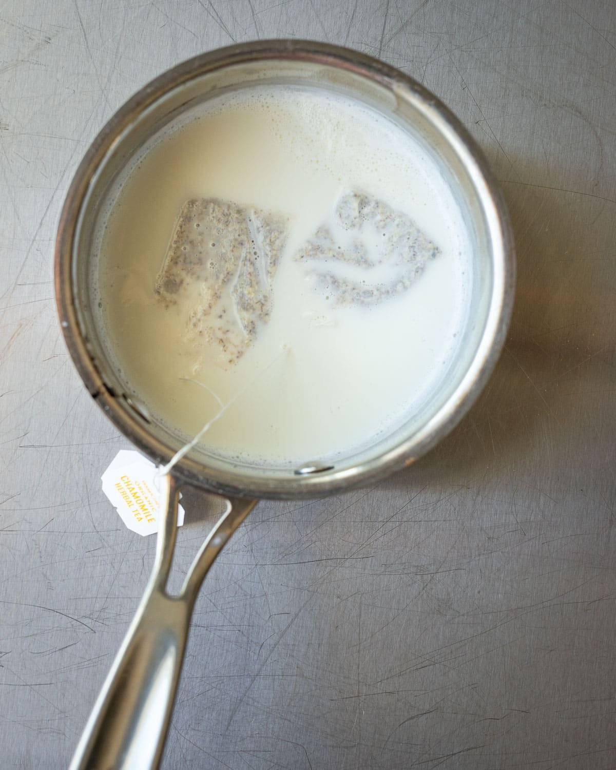 Chamomile tea bags steeping in a small metal pan with milk.